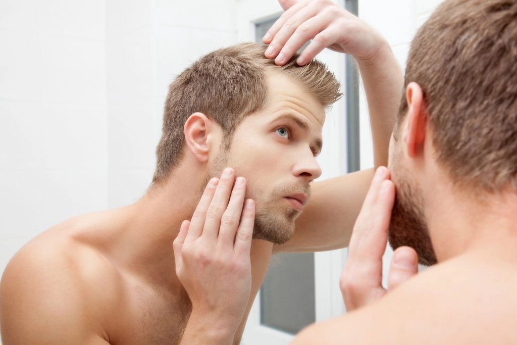 Man standing in front of mirror, worrying about hair loss